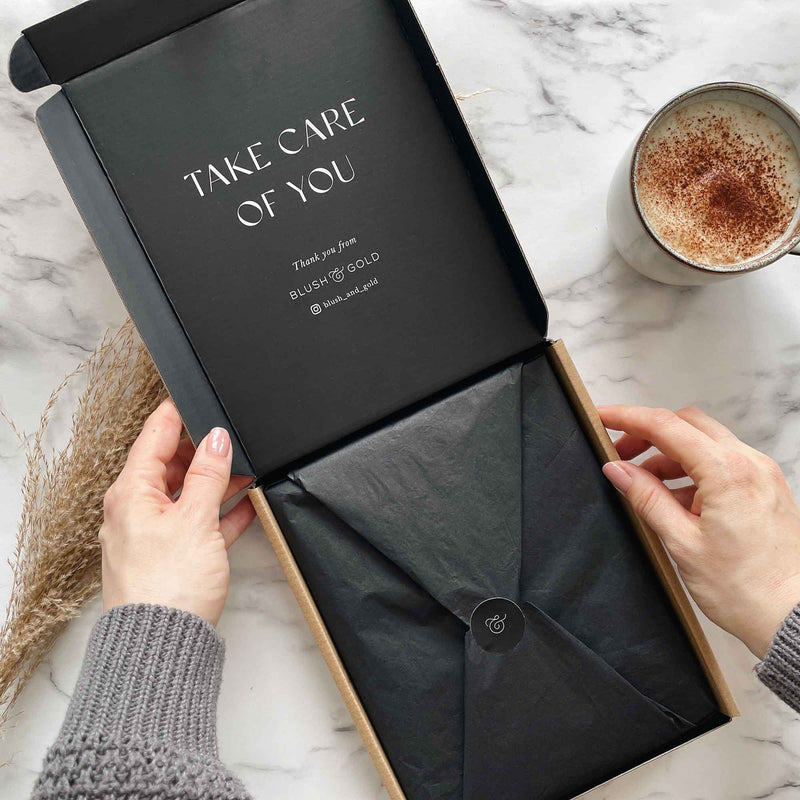 Black box with 'Take Care of You' message on a marble surface with a cup of coffee.