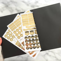 Collection of gold and bronze planner stickers on a black surface