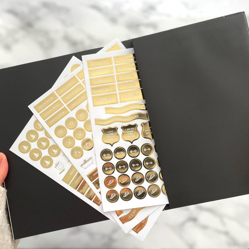 Collection of gold and bronze planner stickers on a black surface