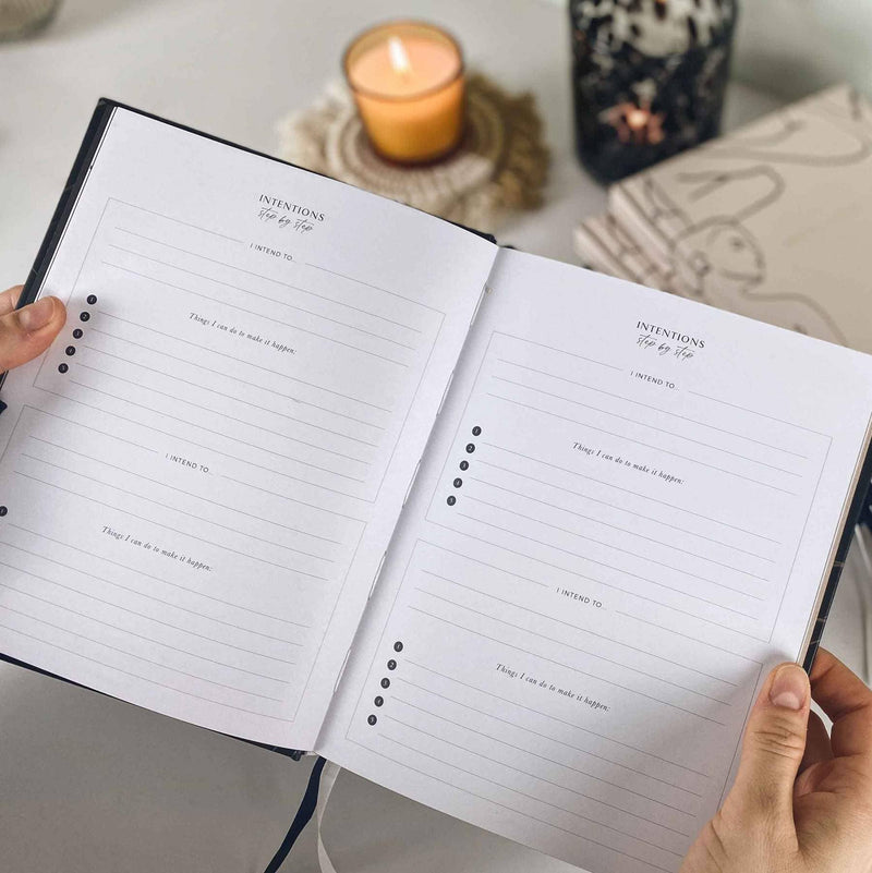 Open notebook with lined pages held by hands, candle in the background