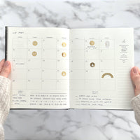 Open planner with celestial designs on a marble surface
