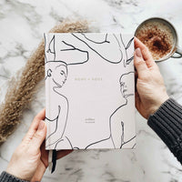 Person holding a planner with line art design on a marble surface with a cup of coffee.
