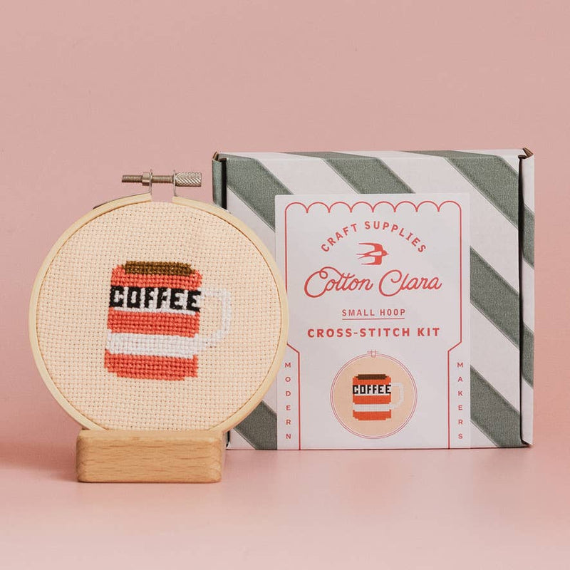Cross-stitch kit with 'Coffee' design and Cotton Clara packaging on a pink background