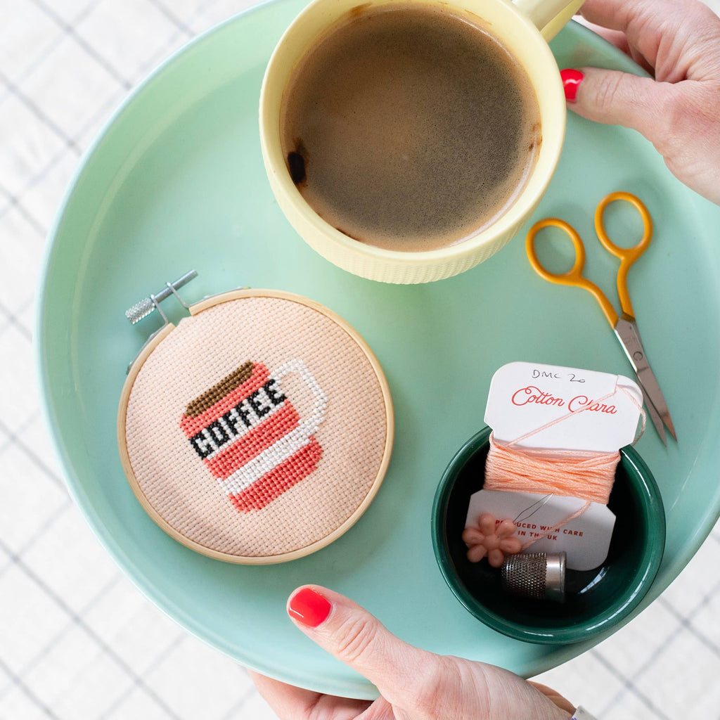 Cross-stitched 'COFFEE' design, a cup of coffee, scissors, and thread.