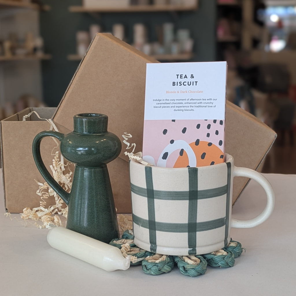 Ceramic mug with plaid design, green candlestick, and tea bag in a box on a table.