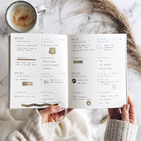 Open planner with daily tasks held by a person with a cup of coffee on a marble surface