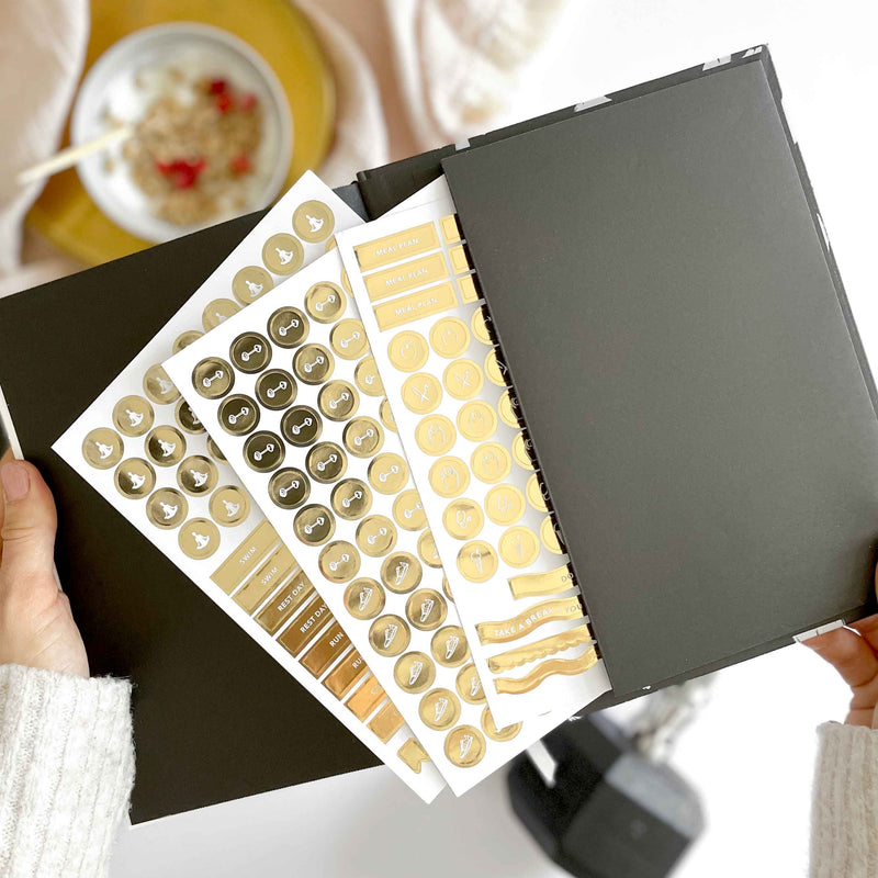 Sheet of decorative stickers with gold and white designs held open by a person.