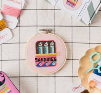 Cross-stitch kit with sardine can design on a checkered surface