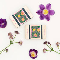 Two small flower presses with floral designs on a white background with flowers around them.