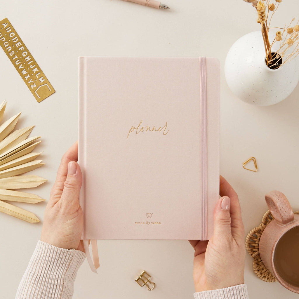 Pink planner held by hands on a light surface with decorative elements