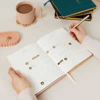 Person using a planner with a cup of coffee and notebooks in the background