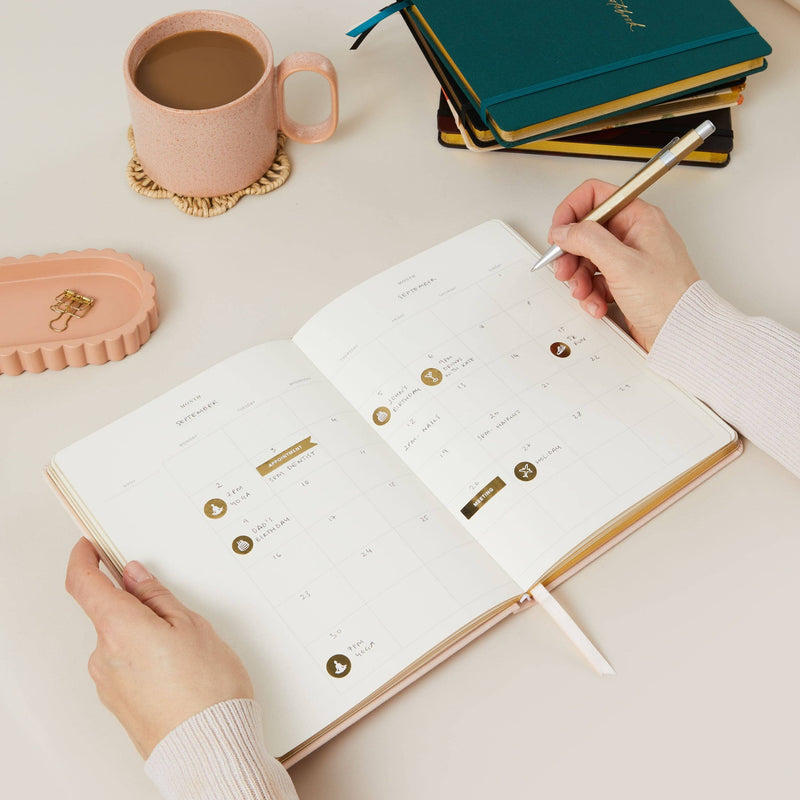 Person using a planner with a cup of coffee and notebooks in the background