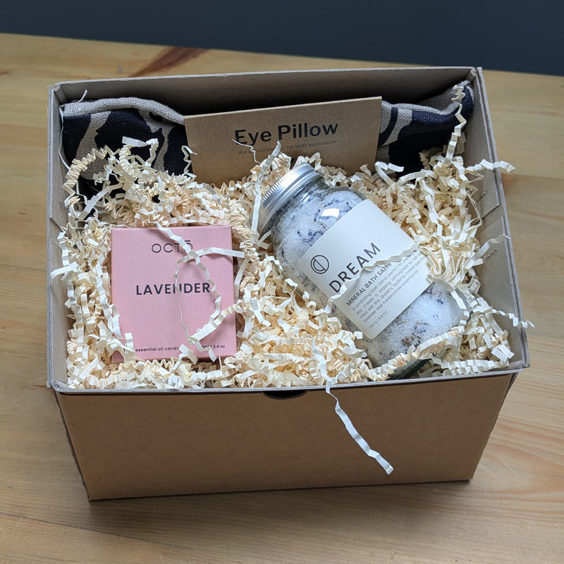 Gift box with bath products including a jar labeled 'Dream', eye pillow, and lavender item on a wooden surface.